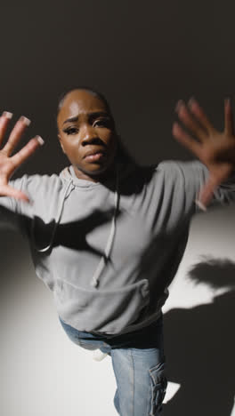 Vertical-Video-Full-Length-Studio-Shot-Of-Young-Woman-Wearing-Hoodie-Dancing-In-Spotlight-With-Shadow-1